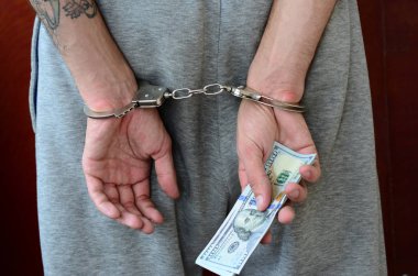 Kelepçeli elleriyle gri pantolon tutuklanan bir adam para büyük miktarda tutar. Arkadan görünüm.