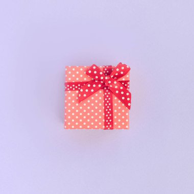 Küçük kırmızı hediye kutusu kurdele ile mor bir arka plan üzerinde yatıyor. Üstten görünüm minimalizm düz yatıyordu.