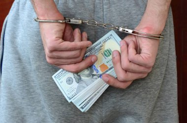 Kelepçeli elleriyle gri pantolon tutuklanan bir adam para büyük miktarda tutar. Arkadan görünüm.