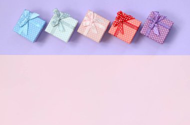 Küçük hediye kutuları farklı renklerde kurdeleler yalanlar üzerine mor ve pembe renkli bir arka planla ile.