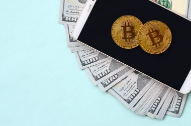 Bir akıllı telefon ve açık mavi arka planı üzerinde yüz dolar faturaları üzerinde Bitcoins yalan.
