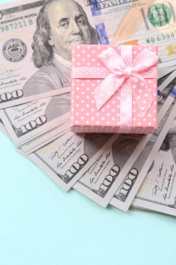 Yüz dolar faturaları üzerinde bir açık mavi renkli yakınındaki pembe noktalı hediye kutusu yatıyor.