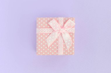 Küçük pembe hediye kutusu kurdele ile mor bir arka plan üzerinde yatıyor. Üstten görünüm minimalizm düz yatıyordu.