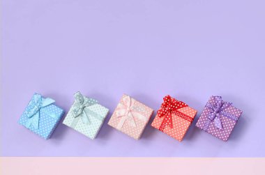 Küçük hediye kutuları farklı renklerde kurdeleler yalanlar üzerine mor ve pembe renkli bir arka planla ile.