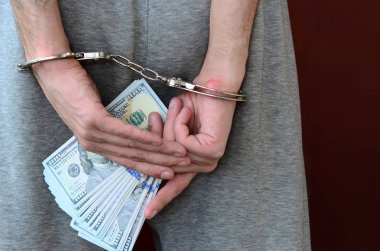 Kelepçeli elleriyle gri pantolon tutuklanan bir adam para büyük miktarda tutar. Arkadan görünüm.