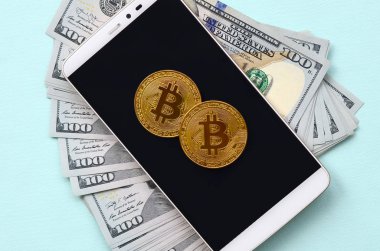 Bir akıllı telefon ve açık mavi arka planı üzerinde yüz dolar faturaları üzerinde Bitcoins yalan.