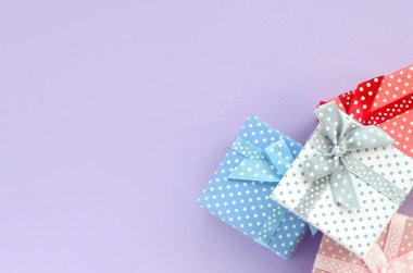 Küçük renkli hediye kutuları şeritler yığını mor bir arka plan üzerinde yatıyor. Üstten görünüm minimalizm düz yatıyordu.