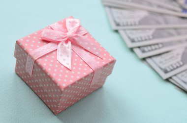 Yüz dolar faturaları üzerinde bir açık mavi renkli yakınındaki pembe noktalı hediye kutusu yatıyor.