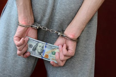 Kelepçeli elleriyle gri pantolon tutuklanan bir adam para büyük miktarda tutar. Arkadan görünüm.