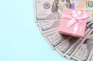 Yüz dolar faturaları üzerinde bir açık mavi renkli yakınındaki pembe noktalı hediye kutusu yatıyor.