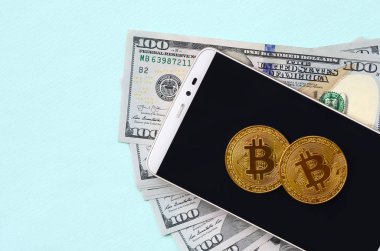 Bir akıllı telefon ve açık mavi arka planı üzerinde yüz dolar faturaları üzerinde Bitcoins yalan.
