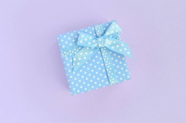 Küçük mavi hediye kutusu kurdele ile mor bir arka plan üzerinde yatıyor. Üstten görünüm minimalizm düz yatıyordu.