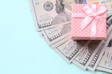Yüz dolar faturaları üzerinde bir açık mavi renkli yakınındaki pembe noktalı hediye kutusu yatıyor.