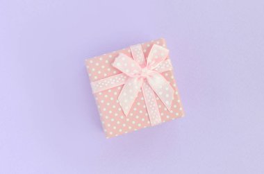 Küçük pembe hediye kutusu kurdele ile mor bir arka plan üzerinde yatıyor. Üstten görünüm minimalizm düz yatıyordu.