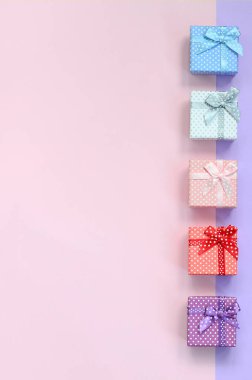 Küçük hediye kutuları farklı renklerde kurdeleler yalanlar üzerine mor ve pembe renkli bir arka planla ile.