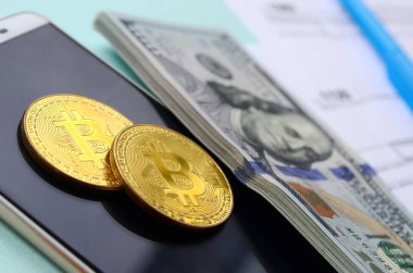 Vergi formları, yüz dolar faturaları ve açık mavi renkli smartphone ile Bitcoins yatıyor. Gelir vergisi beyannamesi.