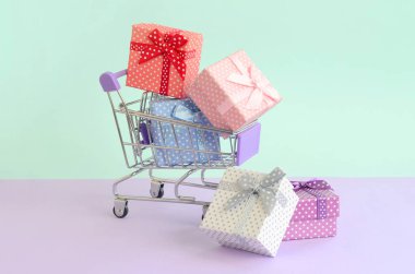 Küçük hediye kutuları farklı renklerde kurdeleler ile mor ve mavi pastel arka plan üzerinde alışveriş sepeti yatıyor.