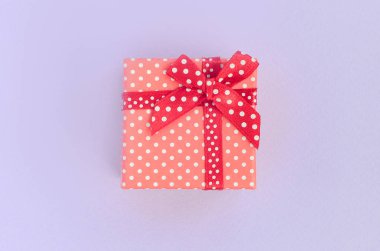 Küçük kırmızı hediye kutusu kurdele ile mor bir arka plan üzerinde yatıyor. Üstten görünüm minimalizm düz yatıyordu.