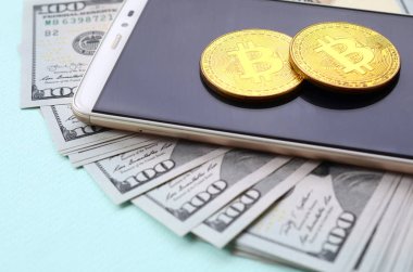 Bir akıllı telefon ve açık mavi arka planı üzerinde yüz dolar faturaları üzerinde Bitcoins yalan.