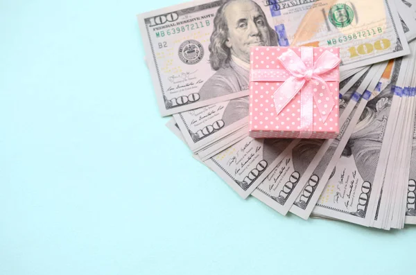 Yüz dolar faturaları üzerinde bir açık mavi renkli yakınındaki pembe noktalı hediye kutusu yatıyor.