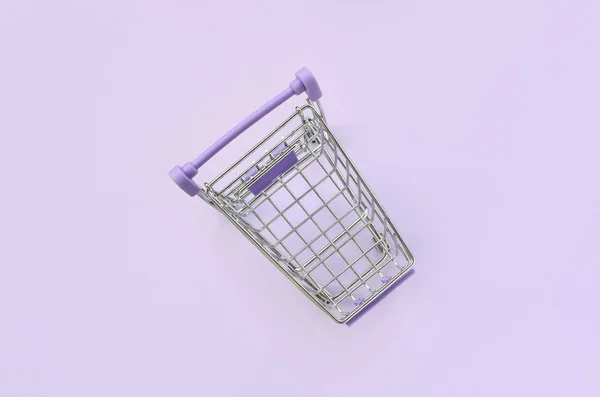 小さなショッピング カートは 紫色の背景にあります ミニマリズム フラット レイアウト平面図 — ストック写真