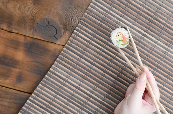 Ręka Pałeczkami Trzyma Sushi Rolkę Bambusowym Słomkowym Tle Maty Żucia — Zdjęcie stockowe