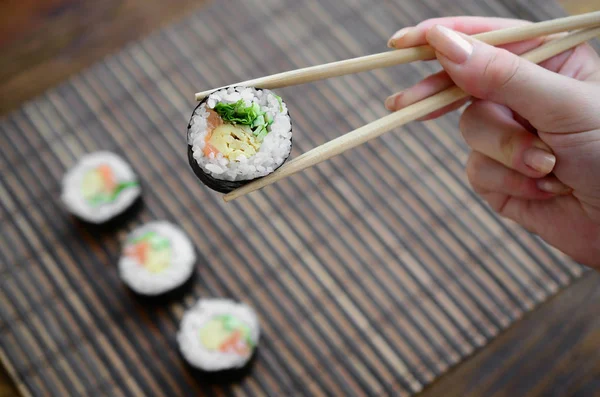 Una Mano Con Bacchette Tiene Rotolo Sushi Uno Sfondo Paglia — Foto Stock