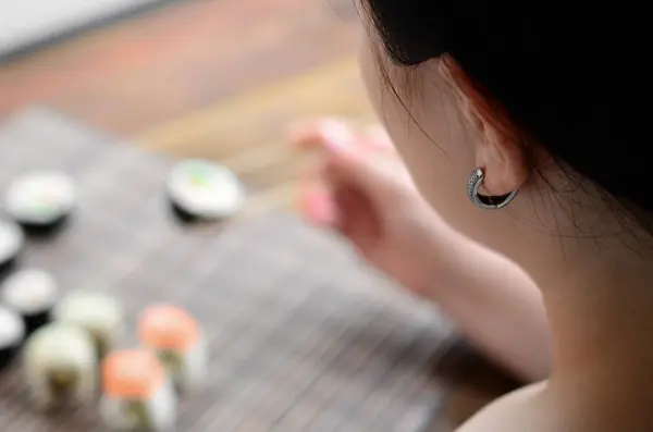 黑头发的女孩用筷子举行寿司卷在竹秸秆 Serwing 垫背景 传统亚洲食品 — 图库照片