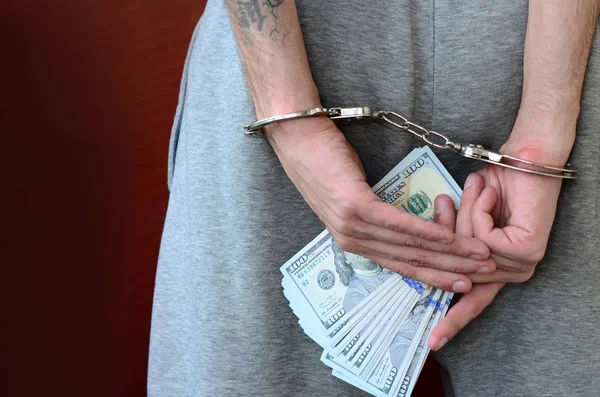 Kelepçeli elleriyle gri pantolon tutuklanan bir adam para büyük miktarda tutar. Arkadan görünüm.
