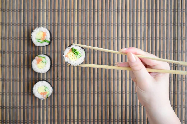 箸を持つ手は 竹のわらの裏に寿司ロールを保持しています 伝統的なアジア料理 — ストック写真