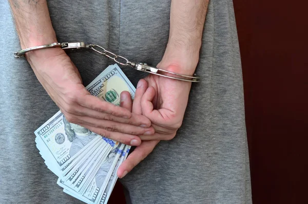 Kelepçeli elleriyle gri pantolon tutuklanan bir adam para büyük miktarda tutar. Arkadan görünüm.