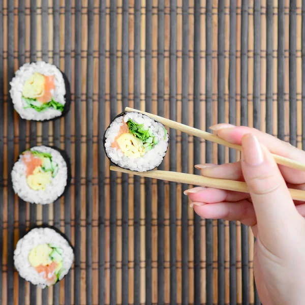 Una Mano Con Bacchette Tiene Rotolo Sushi Uno Sfondo Paglia — Foto Stock