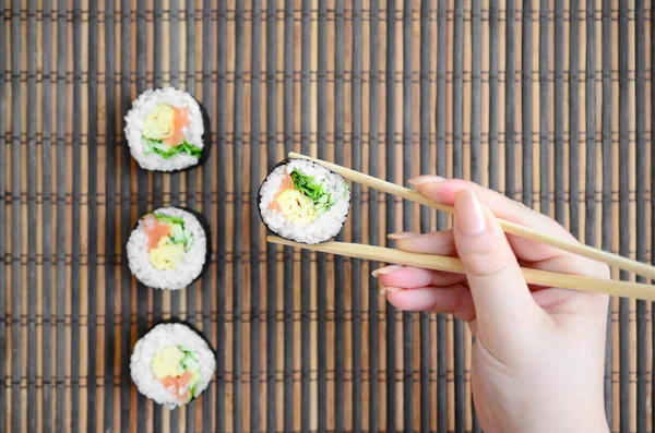 Hand Chopsticks Holds Sushi Roll Bamboo Straw Serwing Mat Background — Stock Photo, Image