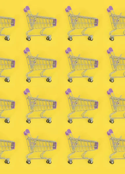 Adicción a las compras, amante de las compras o concepto adicto a las compras. Muchos pequeños carros de compras vacíos realizan un patrón sobre un fondo de papel de color pastel. Composición plana, vista superior — Foto de Stock