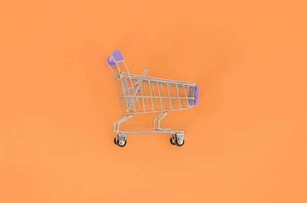 Dipendenza dallo shopping, amante dello shopping o concetto shopaholic. Piccolo carrello vuoto si trova su uno sfondo di carta color pastello. Flat lay composizione minimale, vista dall'alto — Foto Stock