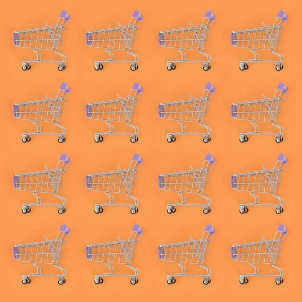 Adicción a las compras, amante de las compras o concepto adicto a las compras. Muchos pequeños carros de compras vacíos realizan un patrón sobre un fondo de papel de color pastel. Composición plana, vista superior — Foto de Stock