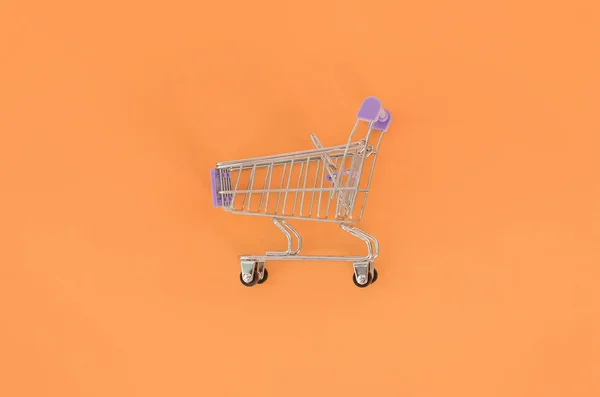 购物成瘾, 购物爱好者或者是购物狂的概念。小的空购物车躺在一个粉彩彩色纸的背景。平躺最小组合, 顶部视图 — 图库照片