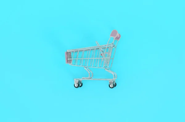 Dipendenza dallo shopping, amante dello shopping o concetto shopaholic. Piccolo carrello vuoto si trova su uno sfondo di carta color pastello. Flat lay composizione minimale, vista dall'alto — Foto Stock