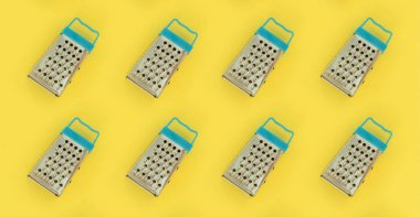 Küçük paslanmaz çelik rende renkli kağıt üzerine pastel yatıyor. Mutfak aksesuarları. Yemek pişirmek için araçlar. Düz yatıyordu üstten görünüm