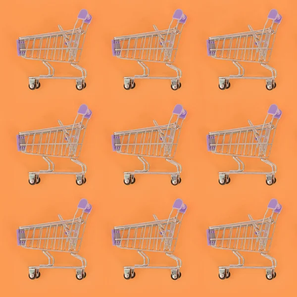 Adicción a las compras, amante de las compras o concepto adicto a las compras. Muchos pequeños carros de compras vacíos realizan un patrón sobre un fondo de papel de color pastel. Composición plana, vista superior — Foto de Stock