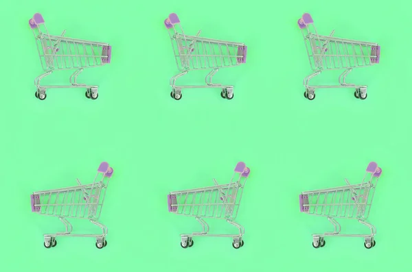 Adicción a las compras, amante de las compras o concepto adicto a las compras. Muchos pequeños carros de compras vacíos realizan un patrón sobre un fondo de papel de color pastel. Composición plana, vista superior —  Fotos de Stock