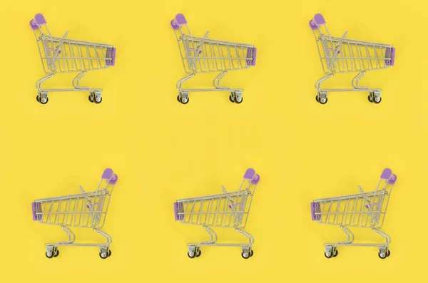 Adicción a las compras, amante de las compras o concepto adicto a las compras. Muchos pequeños carros de compras vacíos realizan un patrón sobre un fondo de papel de color pastel. Composición plana, vista superior — Foto de Stock