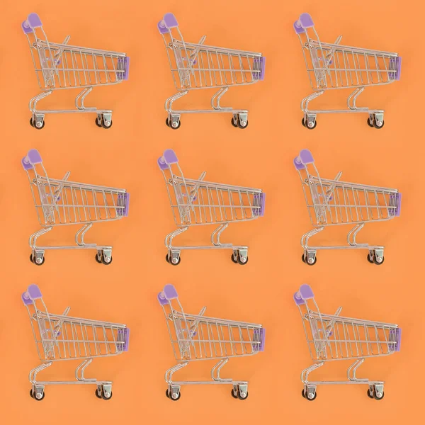 Adicción a las compras, amante de las compras o concepto adicto a las compras. Muchos pequeños carros de compras vacíos realizan un patrón sobre un fondo de papel de color pastel. Composición plana, vista superior — Foto de Stock