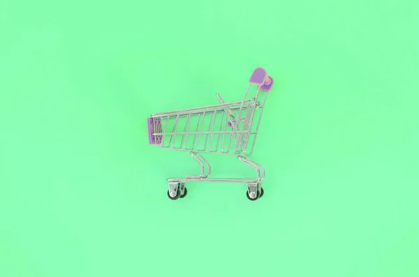 Vício em compras, amante de compras ou conceito shopaholic. Pequeno carrinho de compras vazio encontra-se em um fundo de papel de cor pastel. Plana leigos composição mínima, vista superior — Fotografia de Stock