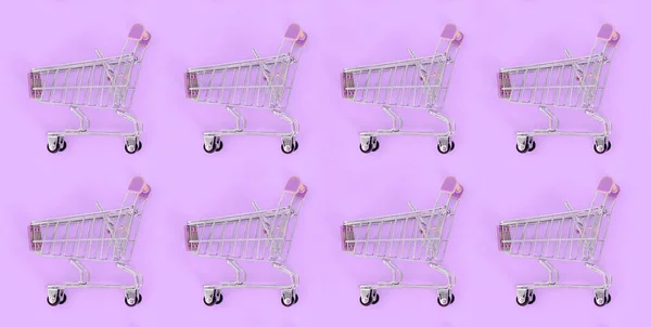 Adicción a las compras, amante de las compras o concepto adicto a las compras. Muchos pequeños carros de compras vacíos realizan un patrón sobre un fondo de papel de color pastel. Composición plana, vista superior — Foto de Stock