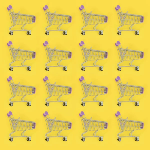 Adicción a las compras, amante de las compras o concepto adicto a las compras. Muchos pequeños carros de compras vacíos realizan un patrón sobre un fondo de papel de color pastel. Composición plana, vista superior — Foto de Stock