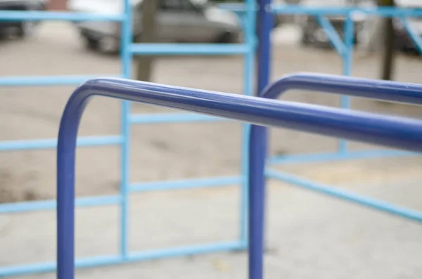 Sports bars in blue on the background of a street sports ground for training in athletics. Outdoor athletic gym equipment. Macro photo with selective focus and extremely blurred background