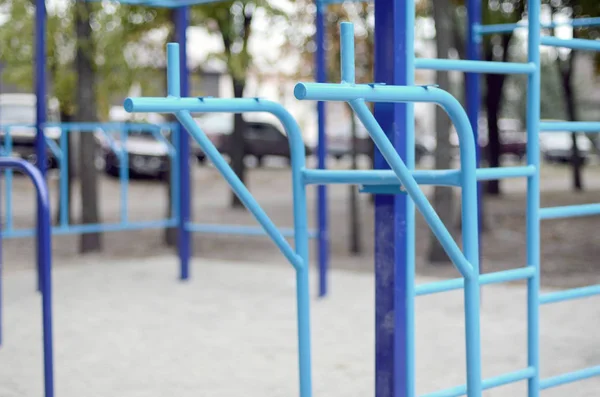 Sports bars in blue on the background of a street sports ground for training in athletics. Outdoor athletic gym equipment. Macro photo with selective focus and extremely blurred background