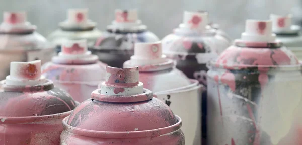 A lot of dirty and used aerosol cans of bright pink paint. Macro photograph with shallow depth of field. Selective focus on the spray nozzle