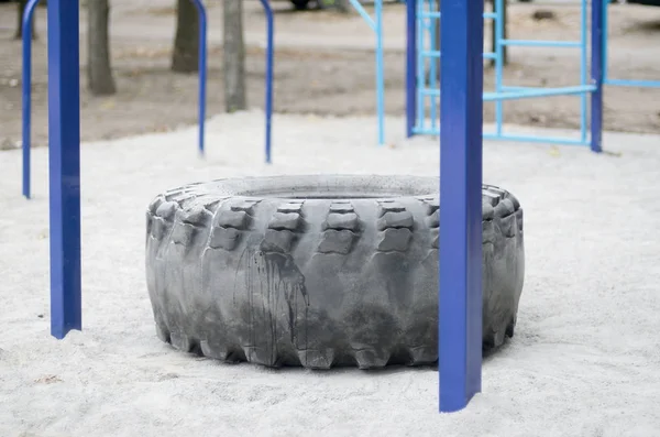A large black tire against a street sports field for training track and field athletics and crossfit. Outdoor athletic gym equipment. Macro photo with selective focus and blurred background